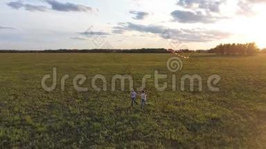 母亲和男孩带着风筝在绿色的田野上奔跑。 欢声笑语，喜庆的心情.. 秋天，日落